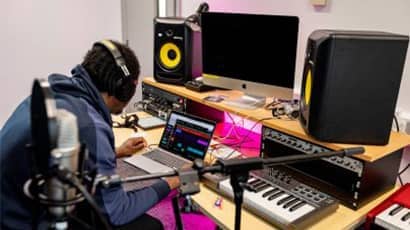 A man working on a laptop on a desk with keyboard, speakers and monitors in the Centre for Music.
