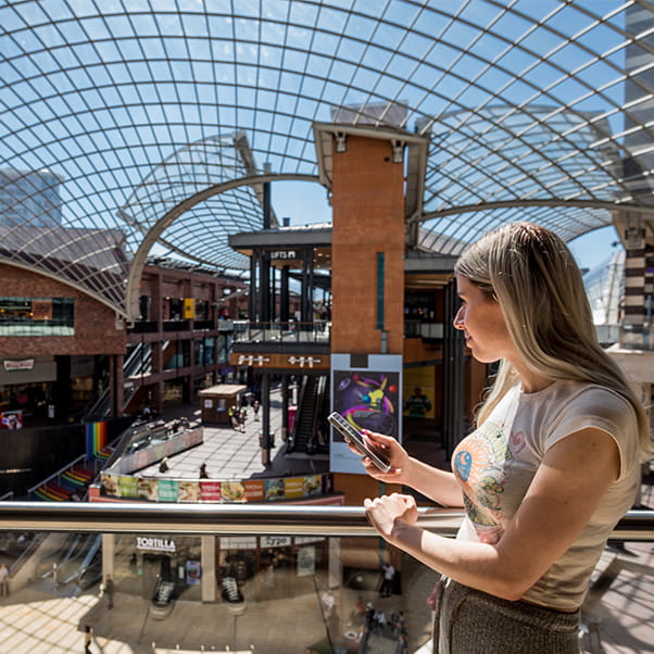 Woman on a balcony looking out over Cabot Circus shopping centre in Bristol.