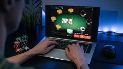 A person sits at a laptop playing poker with gambling chips next to them