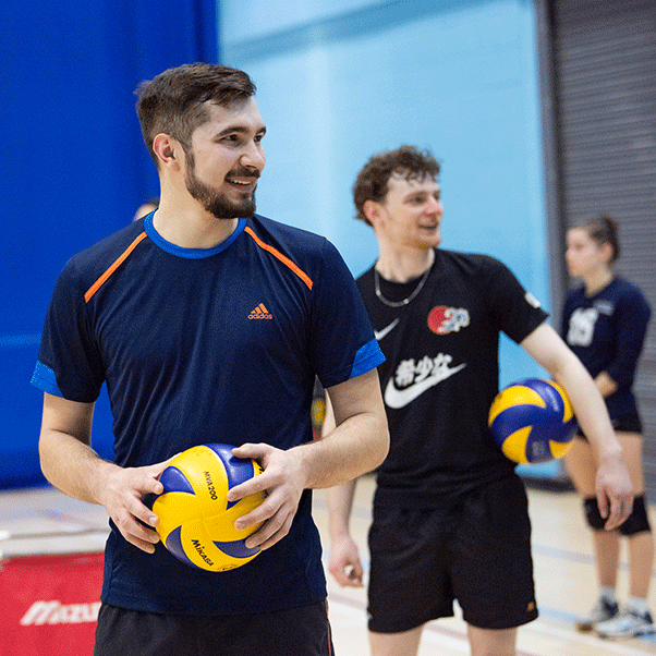 Man looking off camera holding a volleyball in the middle of a game.