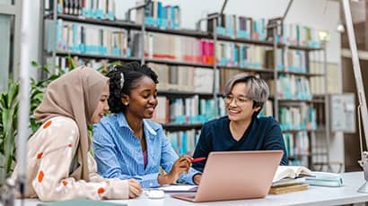 Three students working together at a laptop in a library