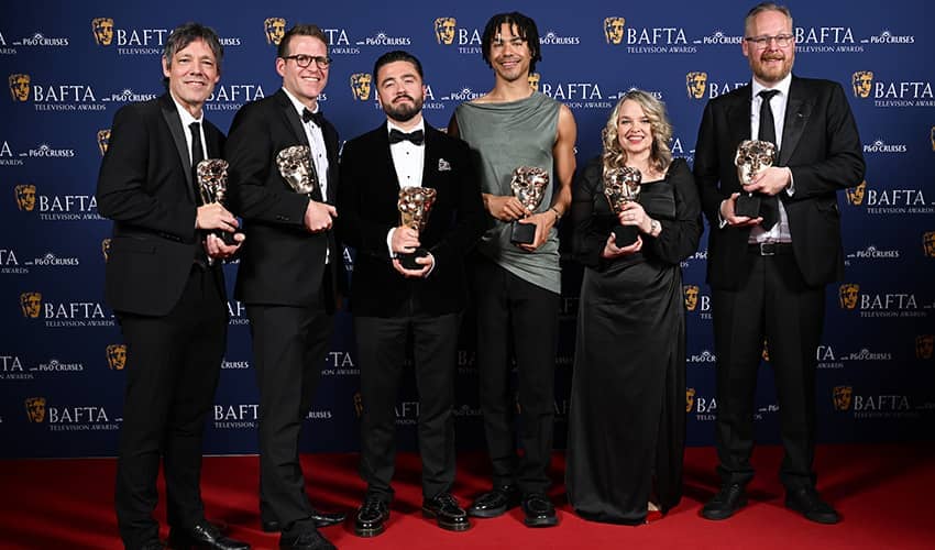 A group of six people holding BAFTA awards smile at the camera