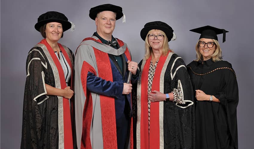 A group of four people wearing ceremonial graduation cap and gowns 