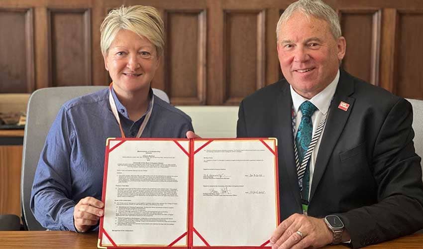 Two people sat at a table holding a signed document towards the camera