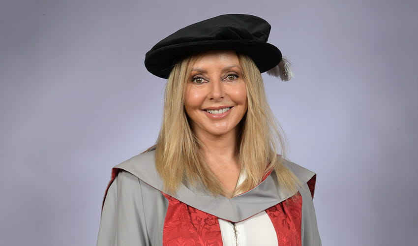 A woman smiling at the camera wearing a black graduation cap and a grey, red and white graduation gown