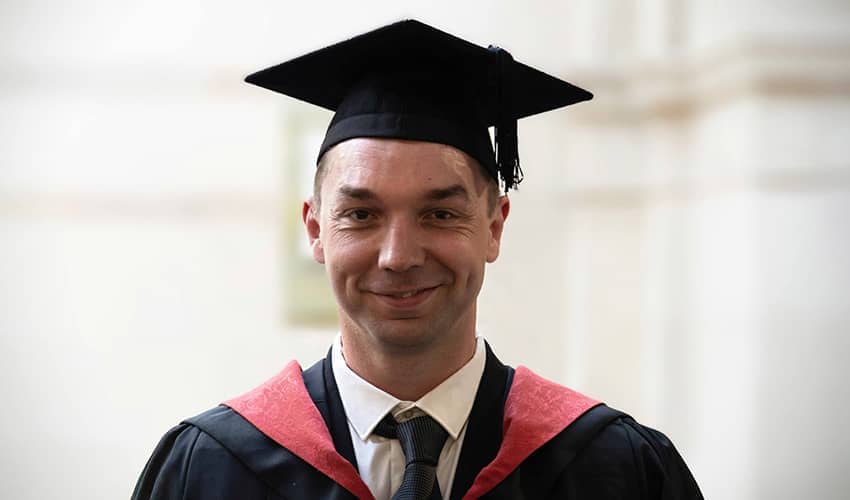 A man smiling at the camera wearing a graduation cap and gown