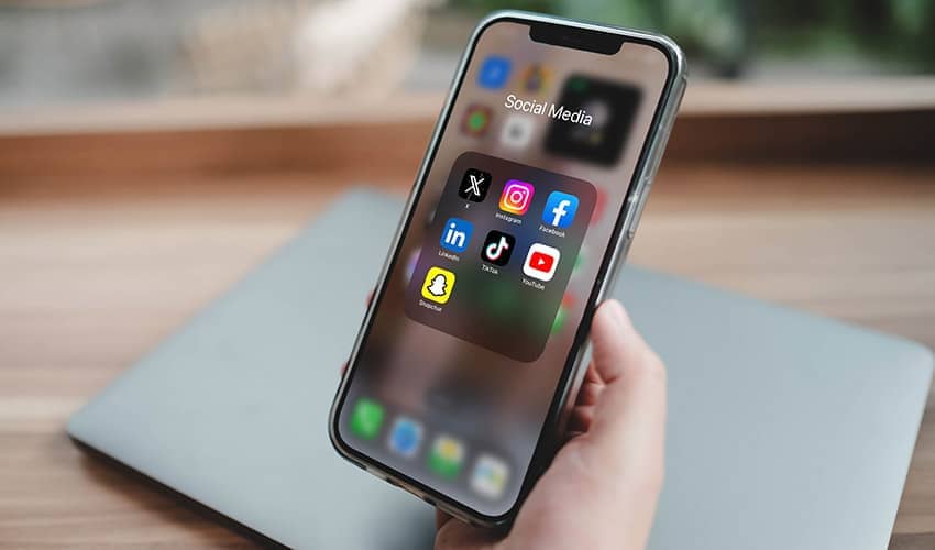 Image of hand holding a smartphone showing social media app icons on the screen