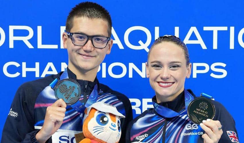 Two swimmers holding up their bronze medals and smiling after competing in a swimming event, with a blue background 