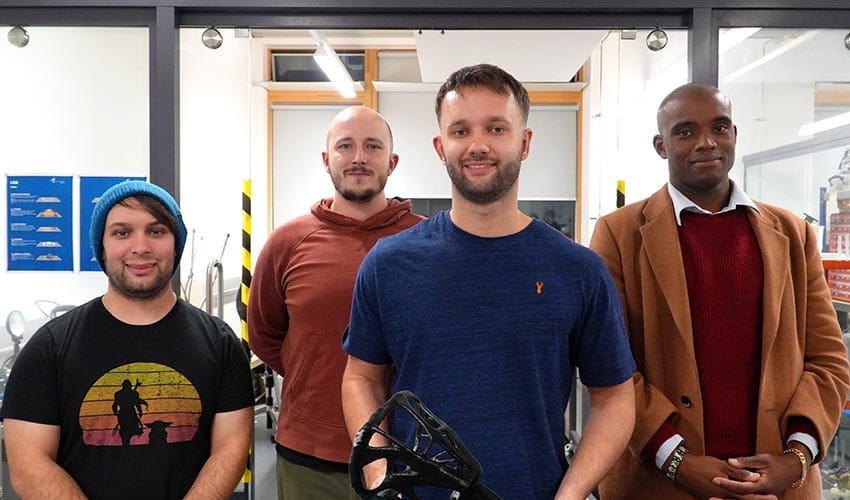 A team photo of four men stood together facing the camera in a mechatronics laboratory at a university