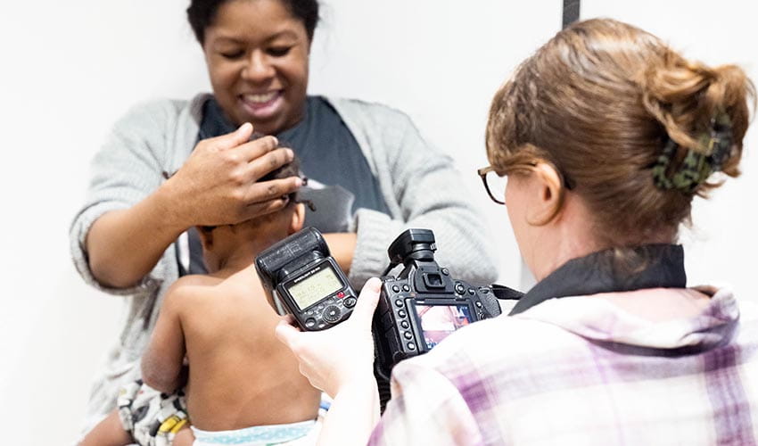 Image showing a female photographer taking a picture of the back of a young child's back, with the child being held by a woman