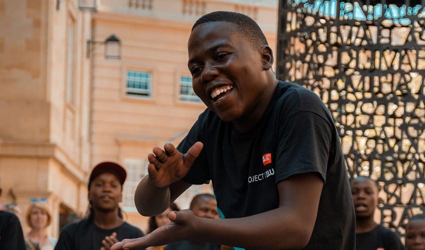 A boy singing and dancing looks at the camera while busking