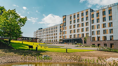 An exterior image of a large block of student accommodation flats with a grass area and small pond in the foreground