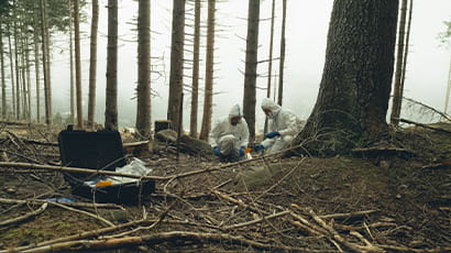 Two scientists wearing white protective hooded suits conduct tests in a forest