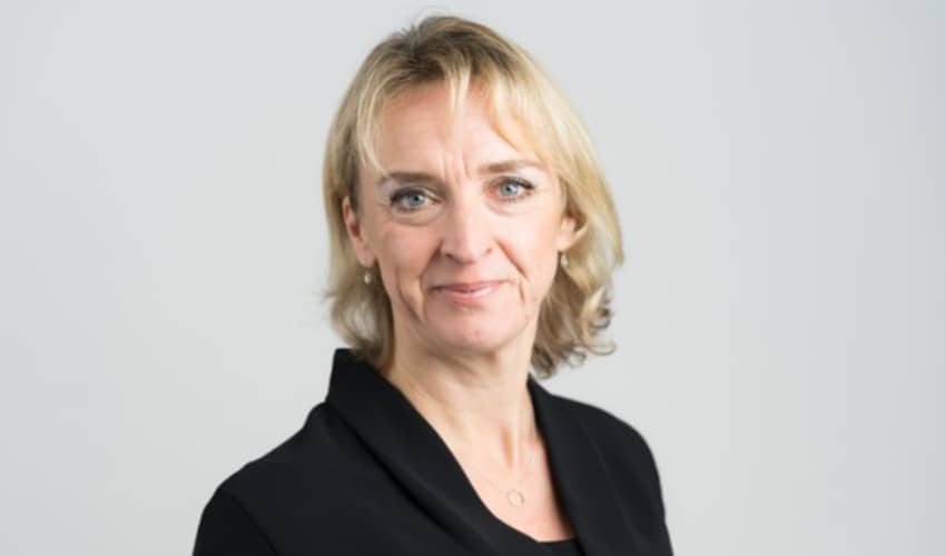 A corporate style headshot of a woman looking directly to camera against a plain grey backdrop. 