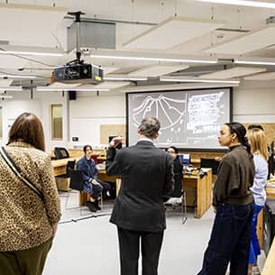 A group of people standing in a large room discussing what is displayed on a large tv screen