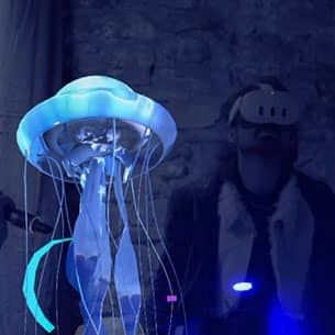 A person wearing a VR headset standing next to a digitally projected jellyfish