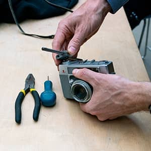 A pair of hands fixing an old camera with tools lying nearby on the a table.