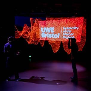 Two people standing on a stage in front of a large LED screen that is displaying the UWE Bristol logo