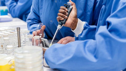 Two people wearing blue gowns conducting research with petri dishes