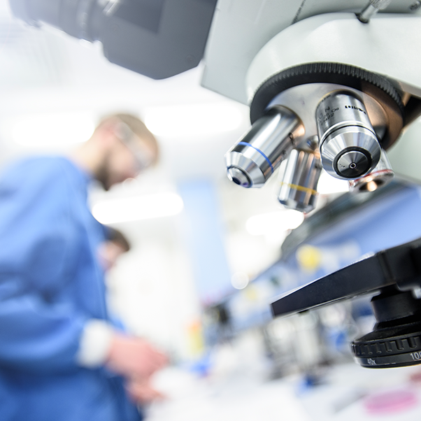 Close up of a microscope with a man in scrubs working in the background.