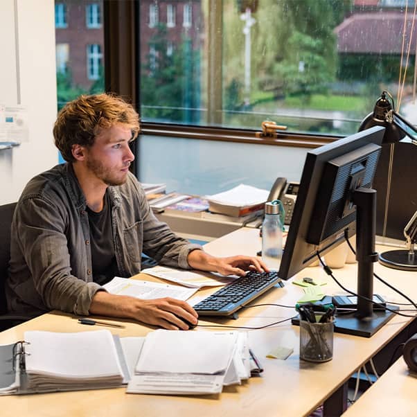 Businessman working at a desk on their computer surrounded by paperwork.