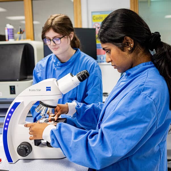 A young adult using a microscope in a lab environment.
