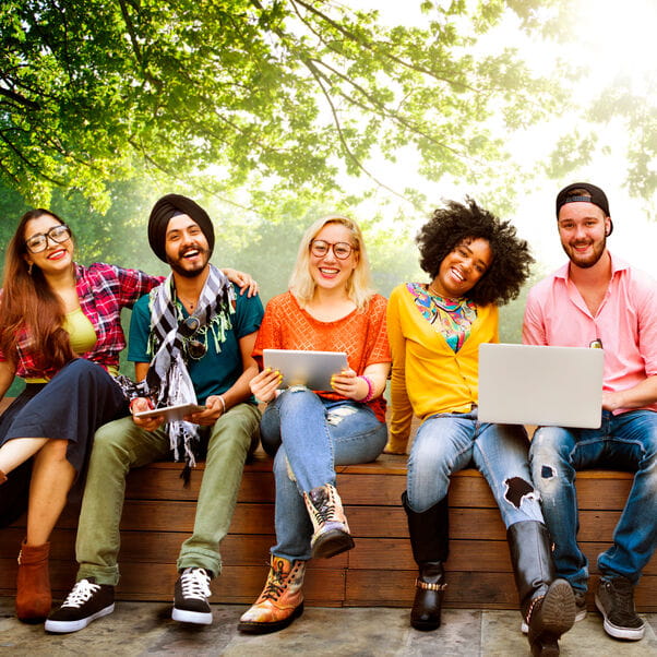 A group of students sitting outside whilst holding different types of mobile devices (laptops and tablets).