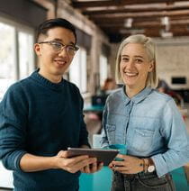 Two staff members greet you with a smile while holding a tablet.