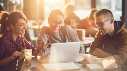 Three students happily looking at a laptop together.