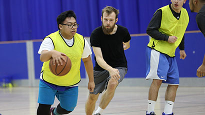 A man dribbles the basketball on court while an opponent player runs to tackle him behind.
